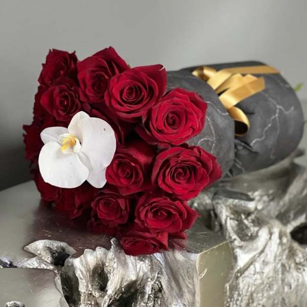 Bouquet of red roses with a white orchid on dark wrapping
