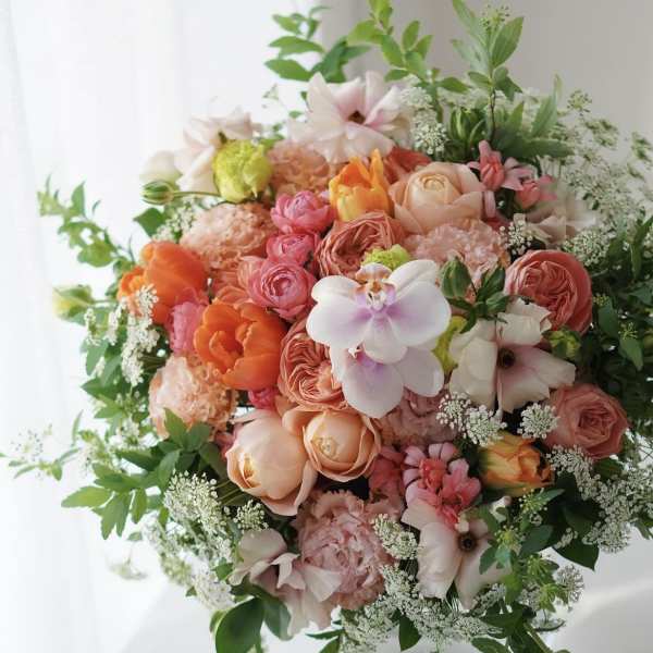 Round bouquet of peach, pink, and white flowers with greenery