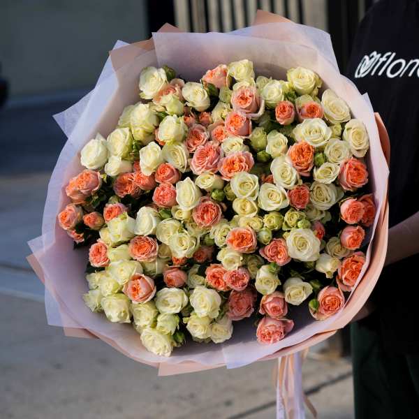 Large bouquet of cream and peach roses wrapped in pink paper