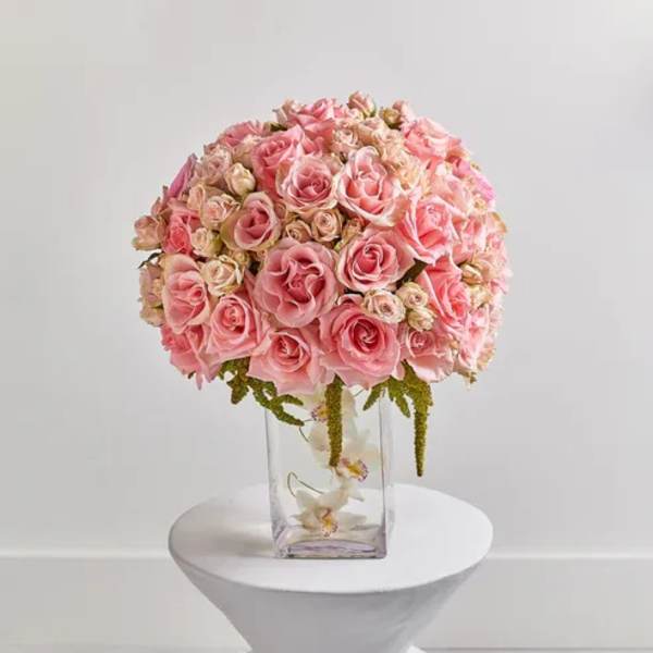 Pink rose bouquet in a clear glass vase on a white pedestal