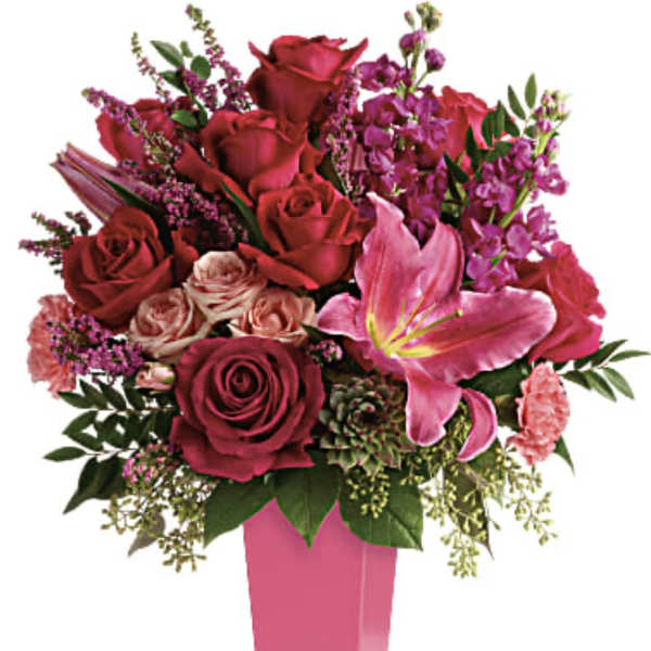 Tall pink vase with red and pink roses, a pink lily, carnations, stock, and a succulent.