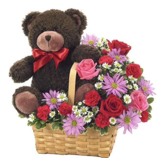 Teddy bear in a basket with mixed pink, red, and purple flowers