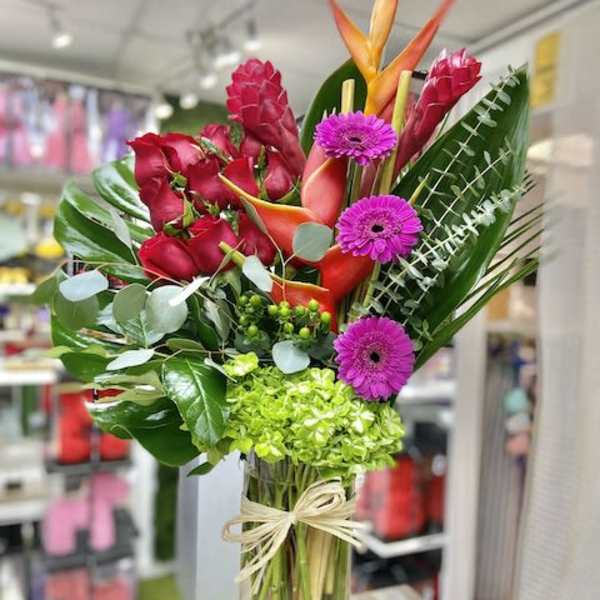 Tall tropical arrangement with red roses, orange blooms, green hydrangea and purple daisies in a glass vase