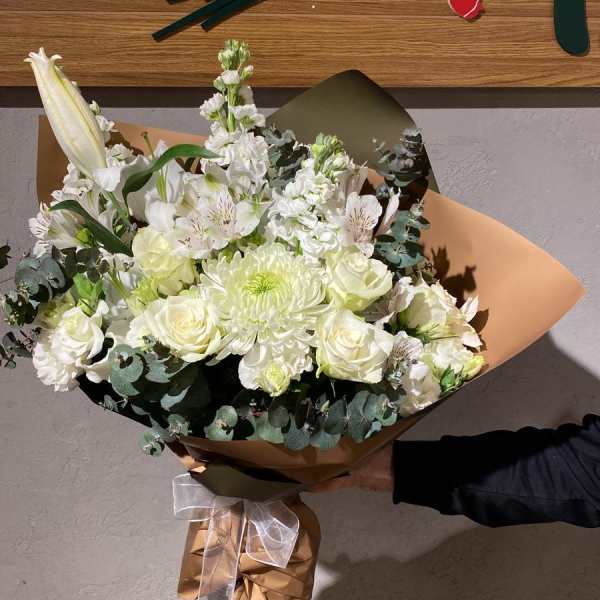 White bouquet with roses, lilies, and chrysanthemums wrapped in brown paper