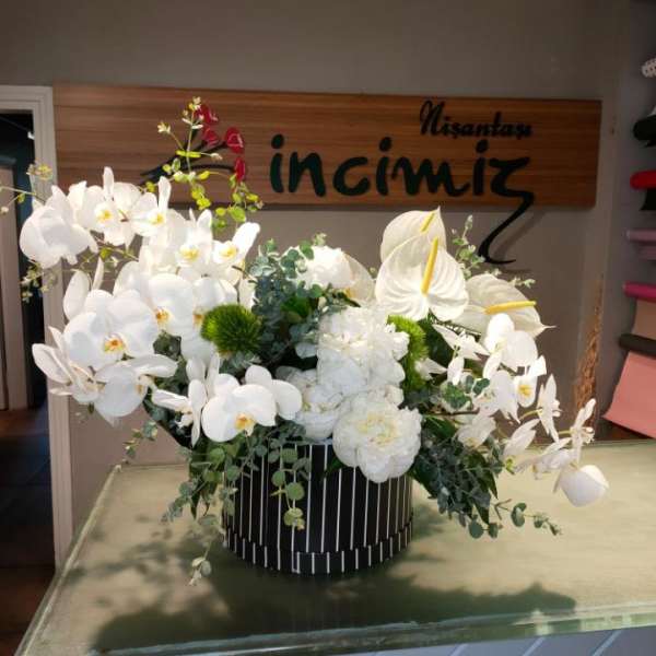 White orchids and anthuriums arranged in a black striped vase