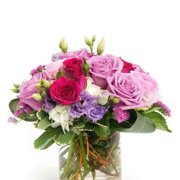 Round arrangement of pink and purple roses with white and lavender blooms in a clear glass vase