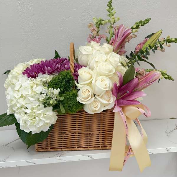 Basket arrangement of white roses, hydrangeas, and pink lilies with ribbon