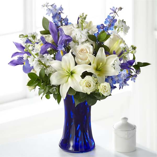 White lilies, roses, and blue-purple flowers in a cobalt vase