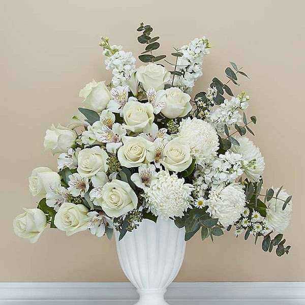 White roses and white flowers arranged in a white urn vase