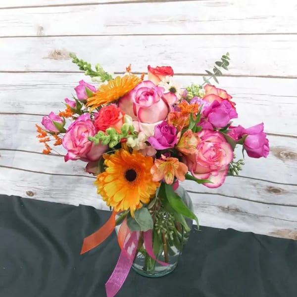 Colorful bouquet of pink roses and orange gerbera daisies in a glass vase