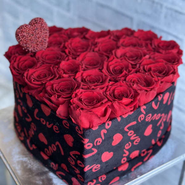 Heart-shaped box filled with red roses and a small heart topper