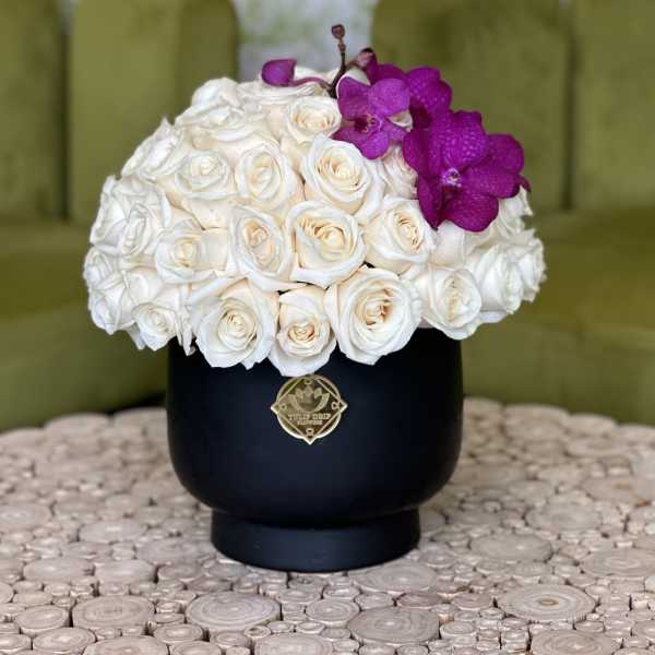 White rose arrangement with purple orchids in a black vase