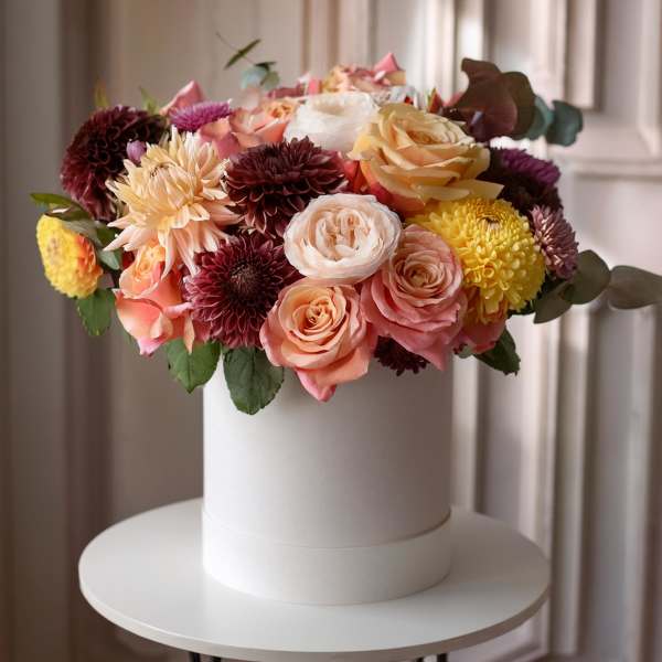 Round bouquet of pink, peach, yellow, and burgundy flowers in a white box