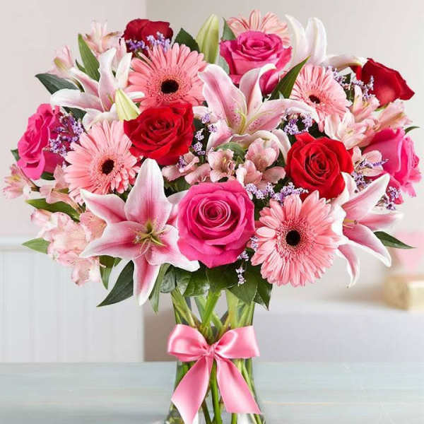 Bouquet of pink and red flowers in a glass vase with a pink ribbon
