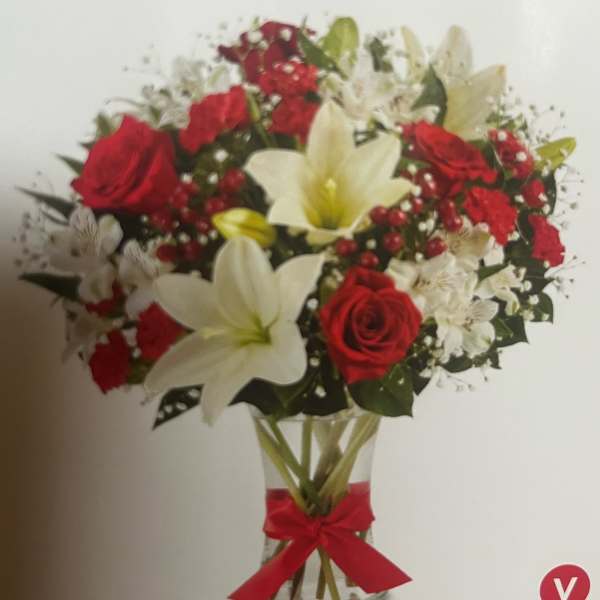 Bouquet of red roses and white lilies in a clear vase with a red ribbon