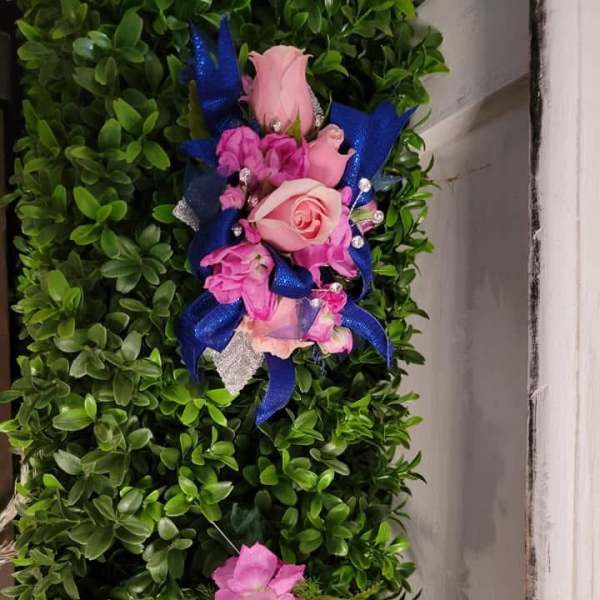 Pink rose corsage with blue ribbon on a green foliage wall