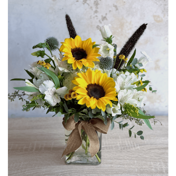 Sunflower arrangement in a clear glass vase with white flowers and a burlap bow