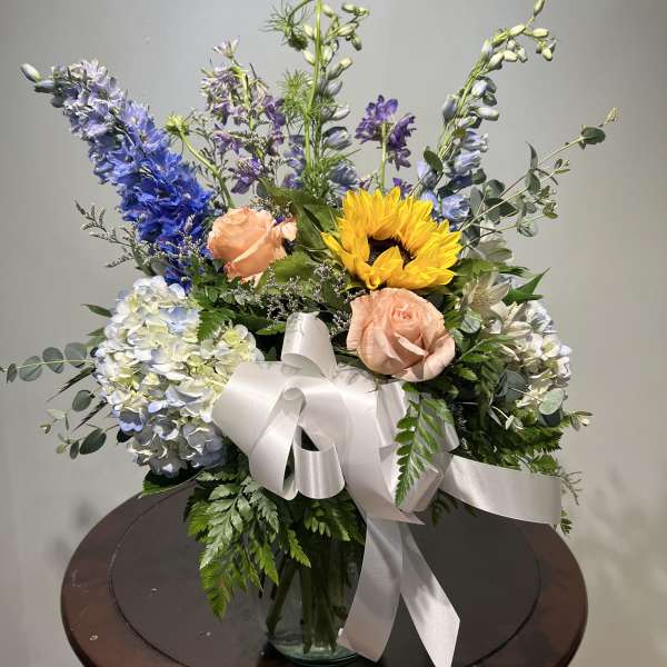 Mixed bouquet with sunflowers, roses, and blue flowers in a glass vase