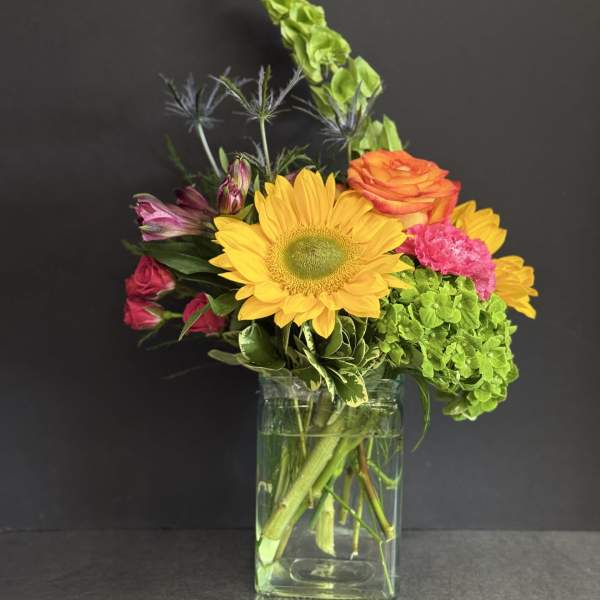 Mixed bouquet with a sunflower, roses, hydrangea, and alstroemeria in a glass vase