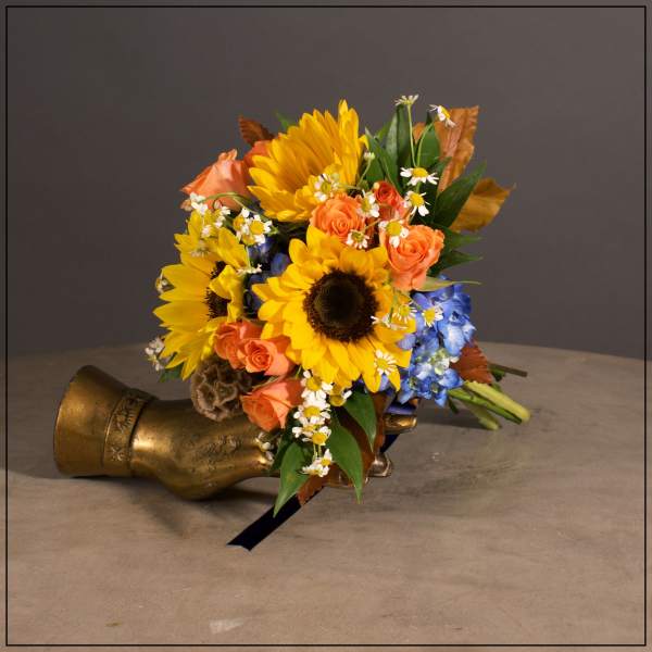 Bouquet of sunflowers, orange roses, and blue flowers beside a brass boot