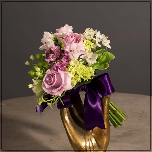 Pink and white bouquet in a gold vase with a purple ribbon