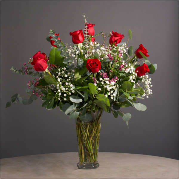 Red roses arranged in a clear glass vase with white filler flowers