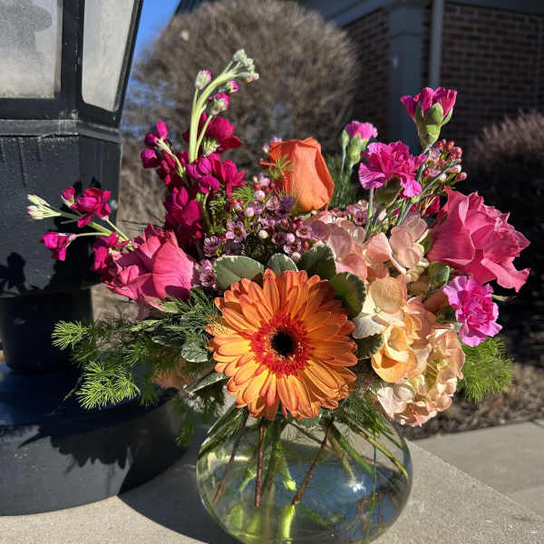 Bright mixed bouquet in a round glass vase with orange and pink blooms