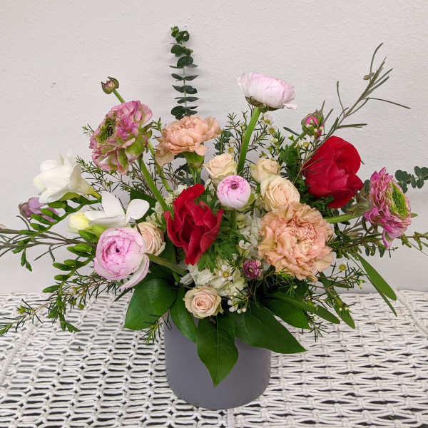 Mixed bouquet of pink, red, and white flowers in a gray vase