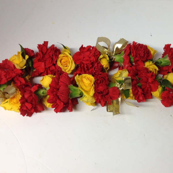 Red and yellow flower garlands with gold ribbon bows on a white surface