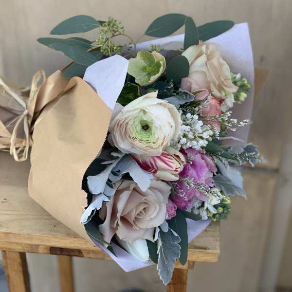 Hand-tied bouquet of pale roses and mixed blooms wrapped in kraft paper