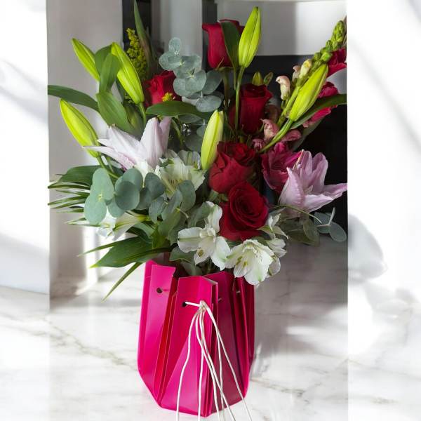 Bouquet of red roses, lilies, and white flowers in a pink gift bag