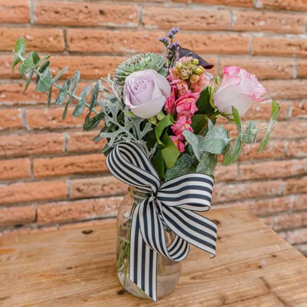 Bouquet of pink and lavender roses in a glass jar with a striped ribbon