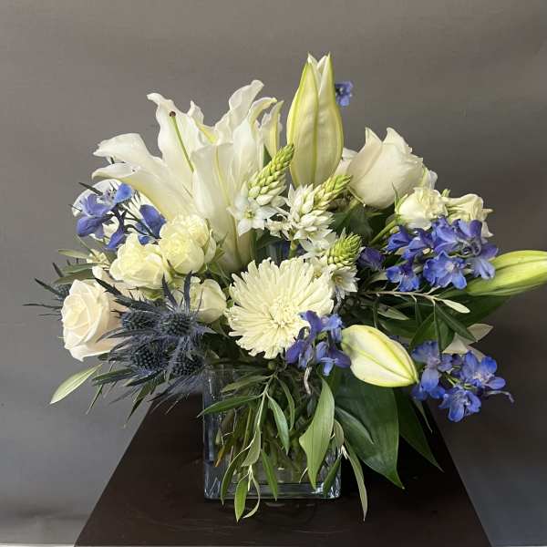 White lilies and roses with blue flowers in a square glass vase