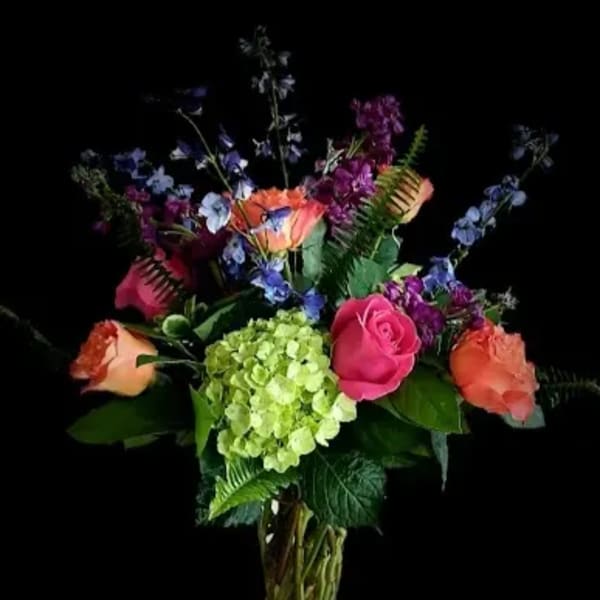 Mixed bouquet of roses, hydrangea, and blue flowers in a glass vase