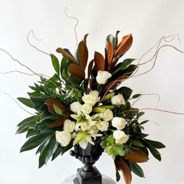 White roses and lilies in a black urn vase with branching twigs