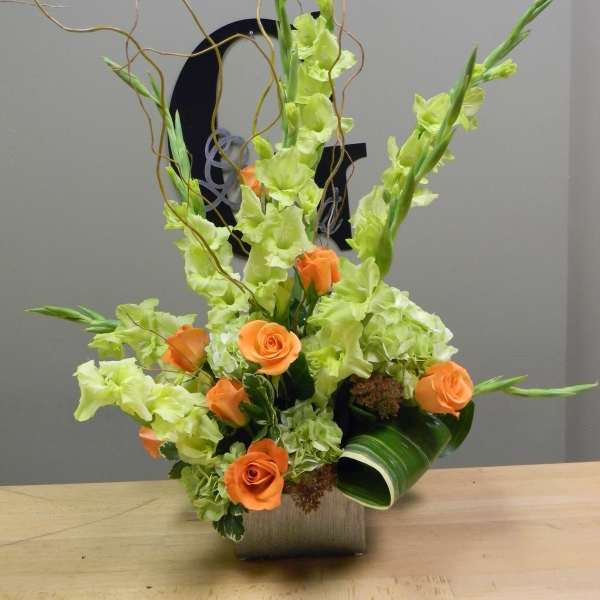 Tall floral arrangement with orange roses and lime-green gladiolus in a square vase