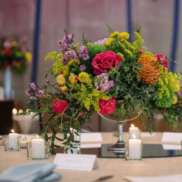 Colorful floral centerpiece in a glass compote with candles around it