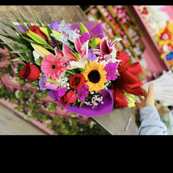 Mixed bouquet with roses, lilies, gerbera daisies, and a sunflower in purple wrap