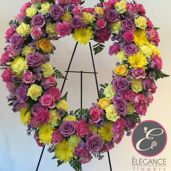 Heart-shaped floral wreath with pink, purple, and yellow blooms on a stand