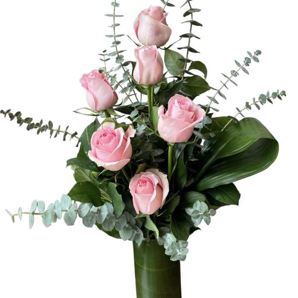 Pink roses arranged in a tall glass vase with eucalyptus foliage