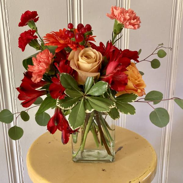 Mixed bouquet of red, orange, and peach flowers in a glass vase