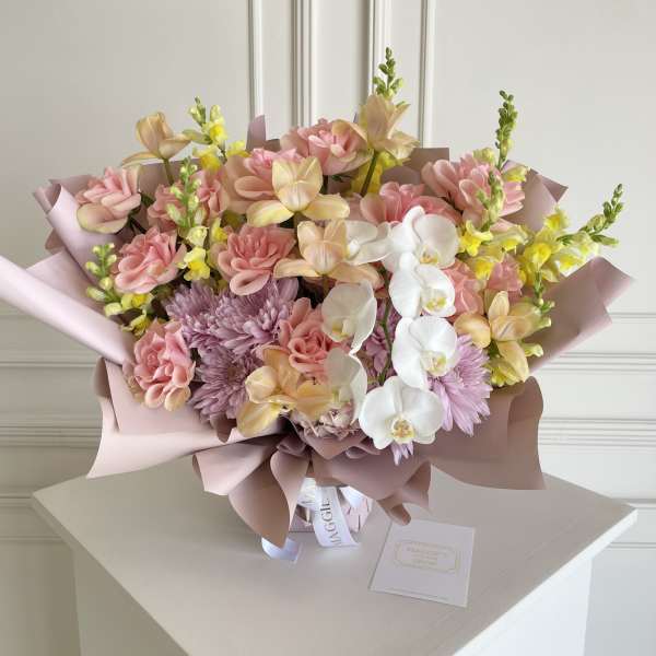 Pastel bouquet with pink roses, orchids, and lavender mums wrapped in blush paper