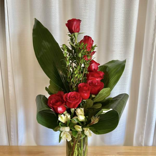 Tall red rose arrangement in a clear glass vase with broad green leaves
