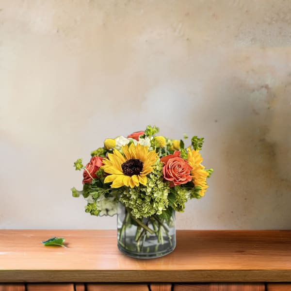Bouquet of sunflowers, roses, and hydrangeas in a glass vase