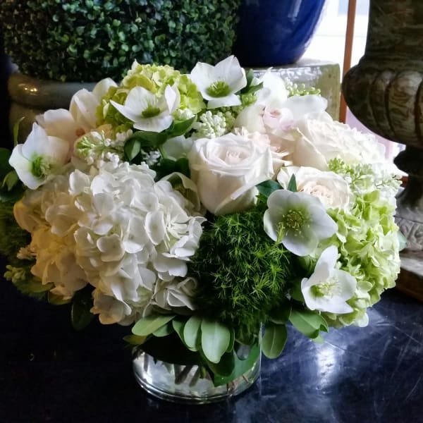 White floral arrangement in a clear glass vase with hydrangeas and roses