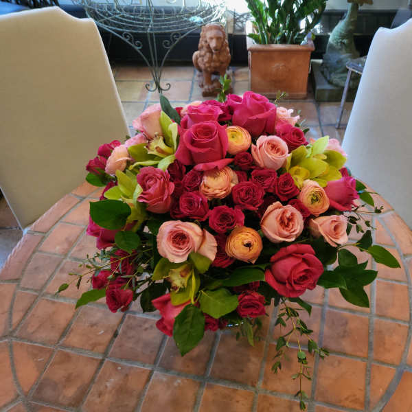 Round bouquet of pink and red roses with green orchids on a table