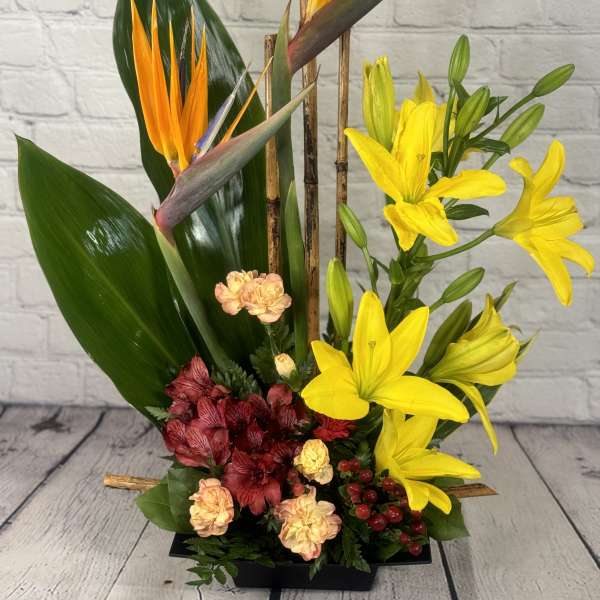Tropical flower arrangement with yellow lilies and bird of paradise in a black container