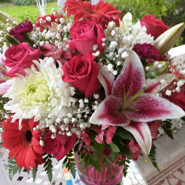 Mixed bouquet of pink roses, lilies, and white chrysanthemums in a glass vase