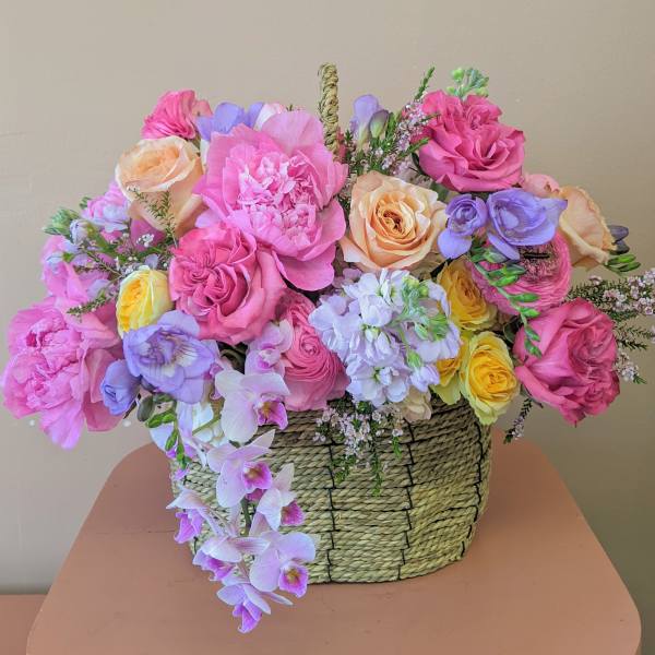 Mixed pink, peach, yellow, and lavender flowers in a woven basket