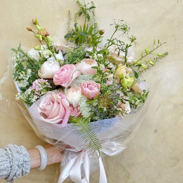 Handheld bouquet of pink and white flowers wrapped in clear paper with a white ribbon